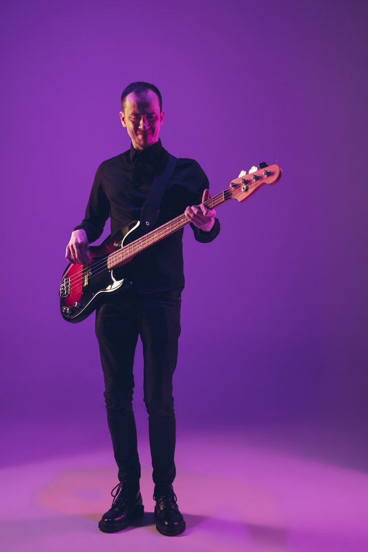 Foto giovane e gioioso musicista caucasico che suona la chitarra su sfondo viola sfumato per studio alla luce al neon. concetto di musica, hobby, festival. ritratto colorato di artista moderno. attento e ispirato.
