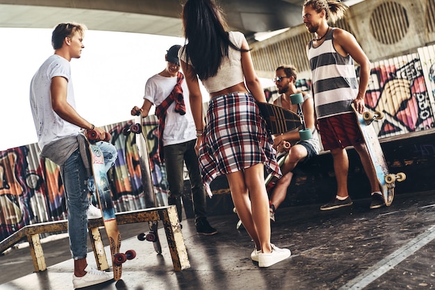 Giovane e pieno di energia. Gruppo di giovani moderni in abbigliamento casual che parlano mentre trascorrono del tempo al parco di skateboard all'aperto