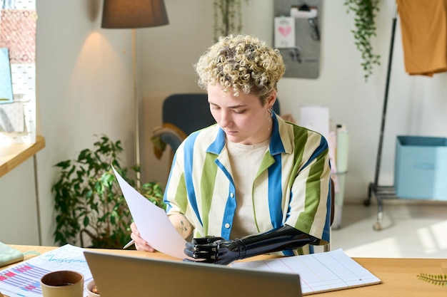 Giovane economista femminile con protesi del braccio che lavora con documenti finanziari