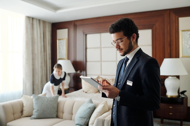 Giovane elegante imprenditore in abiti da cerimonia che utilizza il tablet nella camera d'albergo