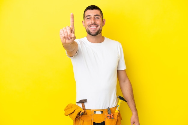 Giovane elettricista uomo caucasico isolato su sfondo giallo che mostra e alza un dito