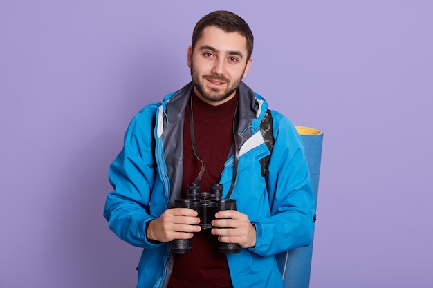 Giovane escursionista barbuto con zaino in piedi e guardando la fotocamera