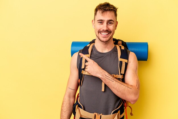 Giovane escursionista uomo caucasico isolato su sfondo giallo sorridente e indicando da parte, mostrando qualcosa in uno spazio vuoto.