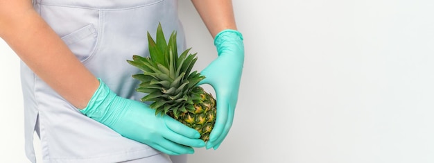 Giovane estetista che indossa guanti blu in uniforme con ananas copre un'area intima su sfondo bianco, concetto di depilazione della zona bikini.