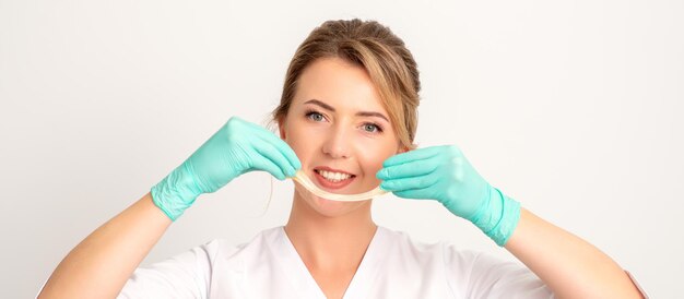 Giovane estetista femmina sorridente caucasica che tiene la cera per la depilazione su sfondo bianco Pasta di zucchero gialla nelle mani maestro della depilazione Concetto di epilazione