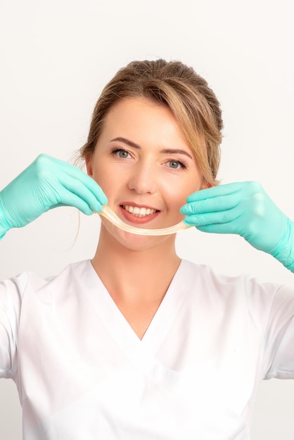 Giovane estetista femmina sorridente caucasica che tiene la cera per la depilazione su sfondo bianco Pasta di zucchero gialla nelle mani maestro della depilazione Concetto di epilazione