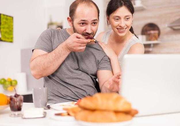 Giovane famiglia che riceve buone notizie via e-mail al mattino facendo colazione. Imprenditore euforico felicissimo di successo a casa al mattino, vincitore e trionfo degli affari