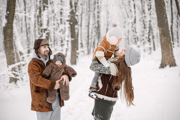 Giovane famiglia con due bambini in piedi nella foresta invernale e in posa per una foto