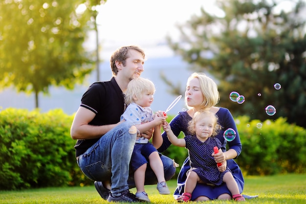 Giovane famiglia con i loro bambini del bambino che soffia bolle di sapone all&#39;aperto in giornata di sole estivo