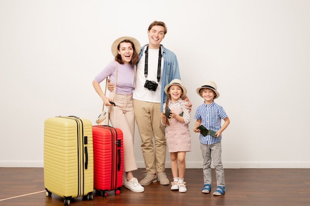 Giovane famiglia entusiasta di due genitori e i loro bambini carini in abbigliamento casual con valigie pronte per il viaggio