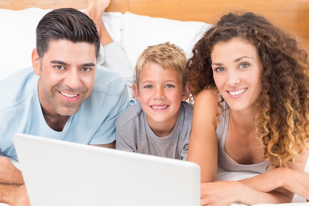 Giovane famiglia felice che per mezzo insieme del computer portatile sul letto