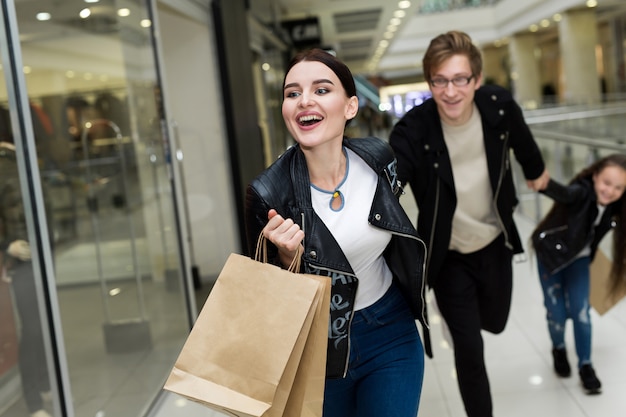 Giovane famiglia felice con i sacchi di carta che compera al centro commerciale. Acquista Windows con vestiti