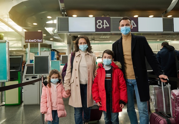 Giovane famiglia felice multirazziale all'aeroporto con bagagli in attesa di un volo in una pandemia. Concetto di viaggio aereo invernale.