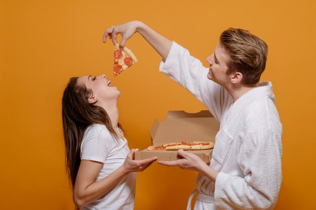 Giovane famiglia in abiti domestici in quarantena con peperoni pizza italiana, si alimentano a vicenda, buoni rapporti familiari, concetto familiare divertente