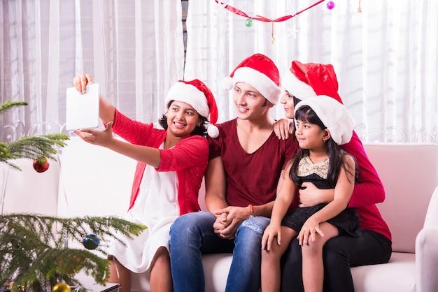 Giovane famiglia indiana asiatica che celebra il Natale con un regalo mentre indossa il cappello di Babbo Natale