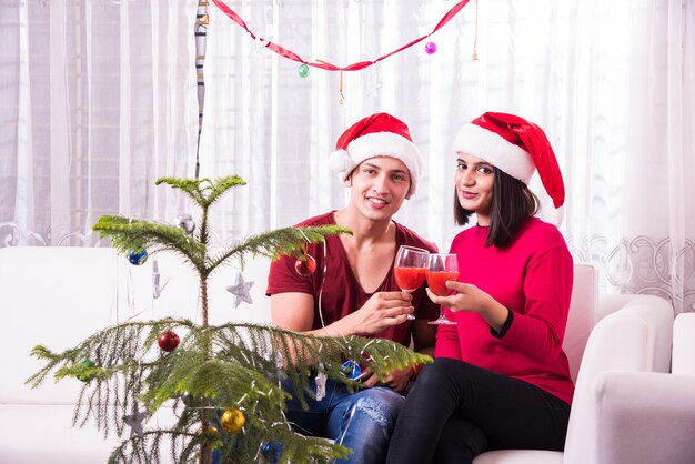 Giovane famiglia indiana asiatica che celebra il Natale con un regalo mentre indossa il cappello di Babbo Natale