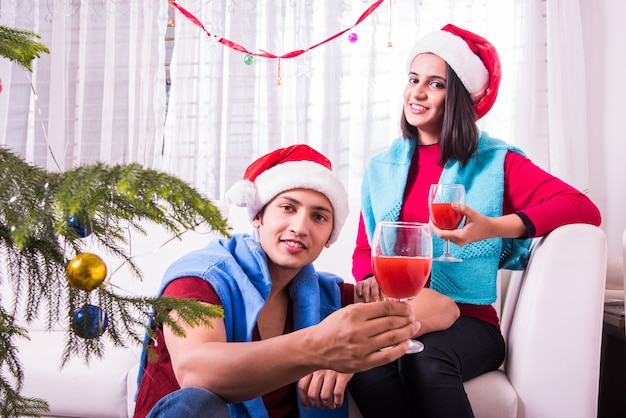 Giovane famiglia indiana asiatica che celebra il Natale con un regalo mentre indossa il cappello di Babbo Natale