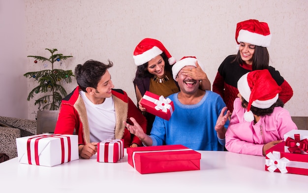 Giovane famiglia indiana asiatica che celebra il Natale con un regalo mentre indossa il cappello di Babbo Natale