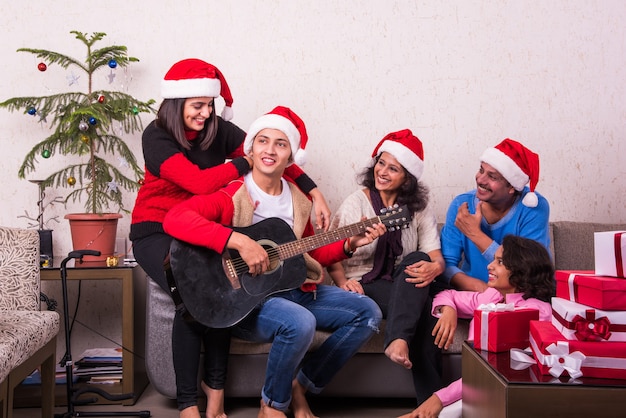 Giovane famiglia indiana asiatica che celebra il Natale con un regalo mentre indossa il cappello di Babbo Natale