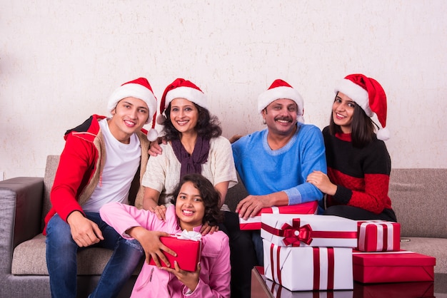 Giovane famiglia indiana asiatica che celebra il Natale con un regalo mentre indossa il cappello di Babbo Natale