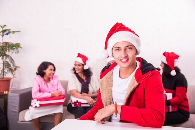 Giovane famiglia indiana asiatica che celebra il Natale con un regalo mentre indossa il cappello di Babbo Natale