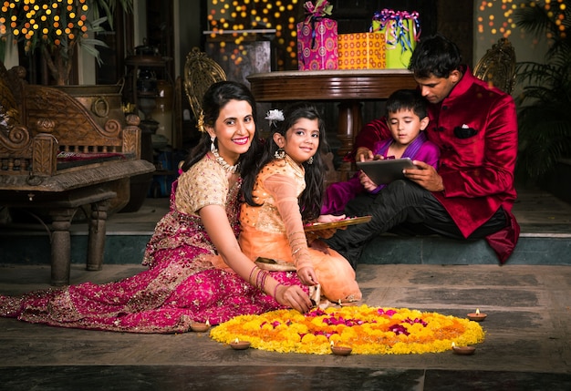 Giovane famiglia indiana che fa fiore Rangoli o organizza diyas per la notte del festival di diwali al portico con doni e bokeh in background