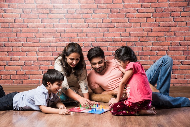 Giovane famiglia indiana di quattro persone che giocano a giochi da tavolo come Chess, Ludo o Snack and Ladder a casa in quarantena