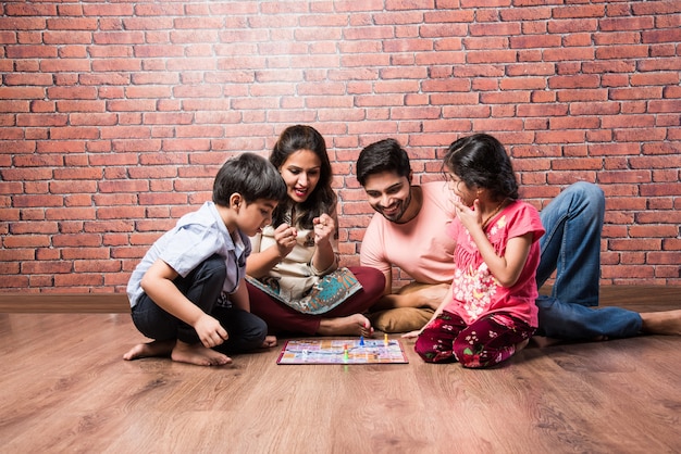 Giovane famiglia indiana di quattro persone che giocano a giochi da tavolo come Chess, Ludo o Snack and Ladder a casa in quarantena