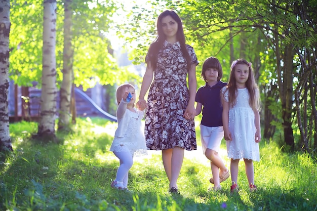 Giovane famiglia numerosa in una passeggiata mattutina estiva. La bella madre con i bambini sta giocando nel parco.