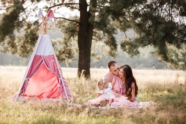 giovane famiglia seduta e divertirsi nel parco estivo vicino al wigwam rosa