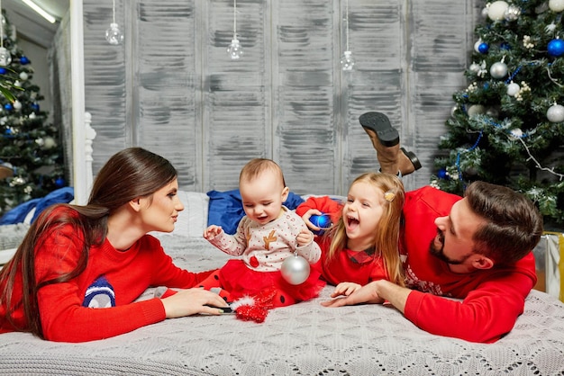 Giovane famiglia sul letto con i bambini sullo sfondo dell'albero di Natale