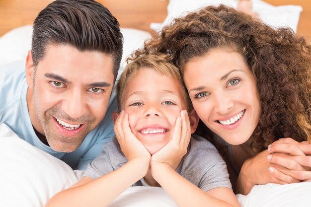 Giovane famiglia sveglia che si trova sul letto che sorride insieme alla macchina fotografica