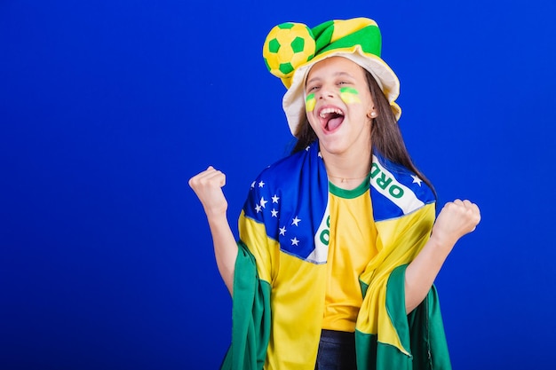 Giovane fan di calcio del Brasile vestito con cappello e bandiera che celebrano