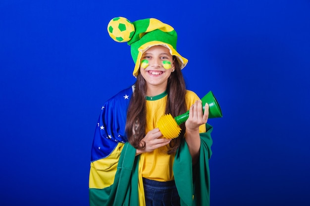 Giovane fan di calcio del Brasile vestito con cappello e bandiera che fa rumore con il clacson