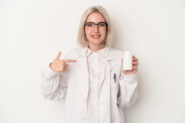 Giovane farmacista donna in possesso di pillole isolate su sfondo bianco persona che punta a mano a uno spazio di copia camicia orgoglioso e fiducioso