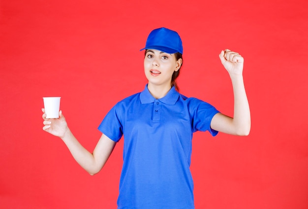 Giovane fattorina in berretto blu in posa con una tazza di tè in plastica sul rosso.