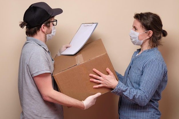 Giovane fattorino in maschera medica che dà un pacco di cartone al cliente