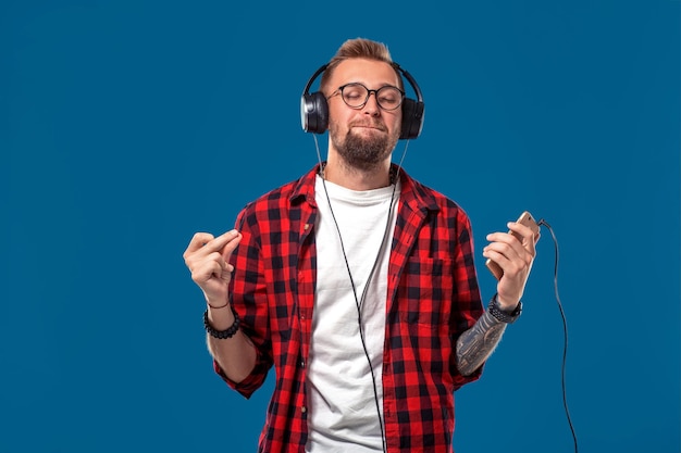 Giovane felice che ascolta la musica con le cuffie bel ragazzo sorridente in camicia a quad...