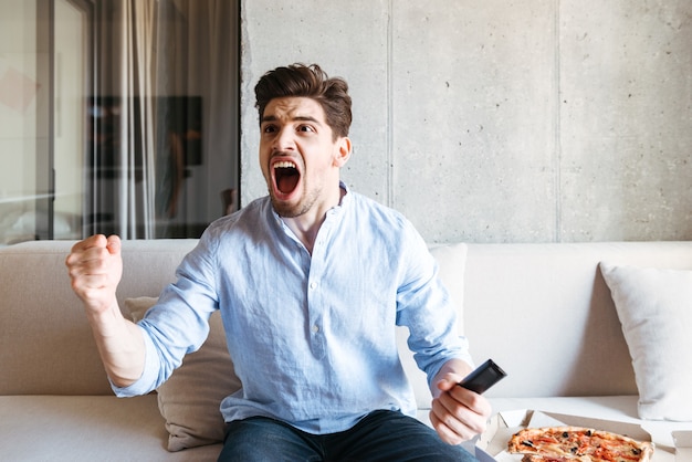 Giovane felice che tiene telecomando della TV e che celebra