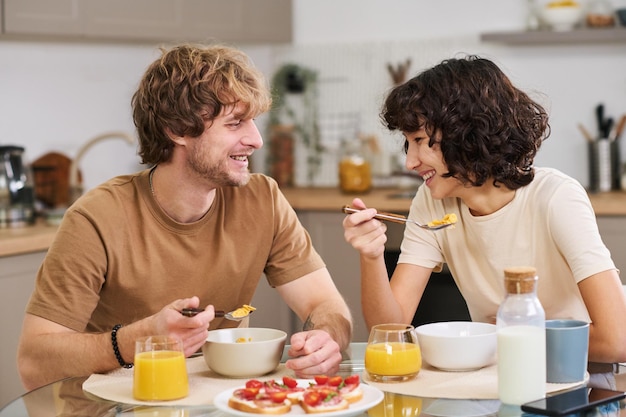 Giovane felice e sua moglie che mangiano cornflakes con latte per colazione