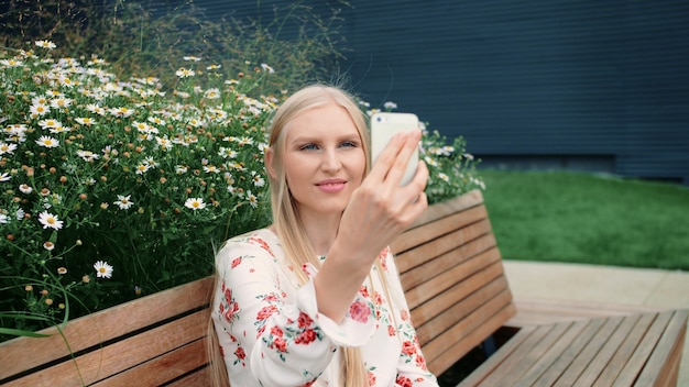 Giovane femmina adorabile che per mezzo dello smartphone per fare videochiamata mentre sedendosi sul banco sul tetto vivente del centro commerciale enorme