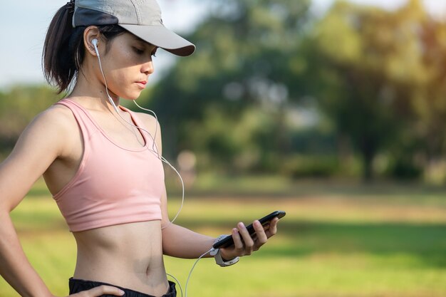 Giovane femmina adulta ascolta musica su smartphone durante la corsa nel parco all'aperto, donna corridore fare jogging al mattino. Concetti di esercizio, tecnologia, stile di vita e allenamento