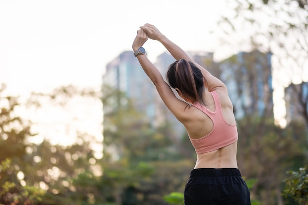 Giovane femmina adulta in abiti sportivi rosa che allunga i muscoli nel parco all'aperto, donna sportiva warm up pronta per correre e fare jogging al mattino. concetti di benessere, fitness, esercizio e equilibrio tra lavoro e vita familiare