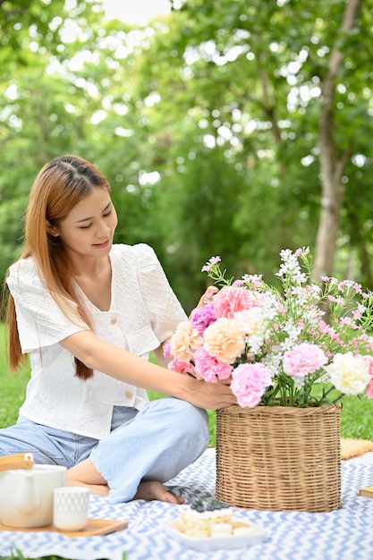 Giovane femmina asiatica attraente che fa un picnic nel giardino che tiene un cesto di fiori