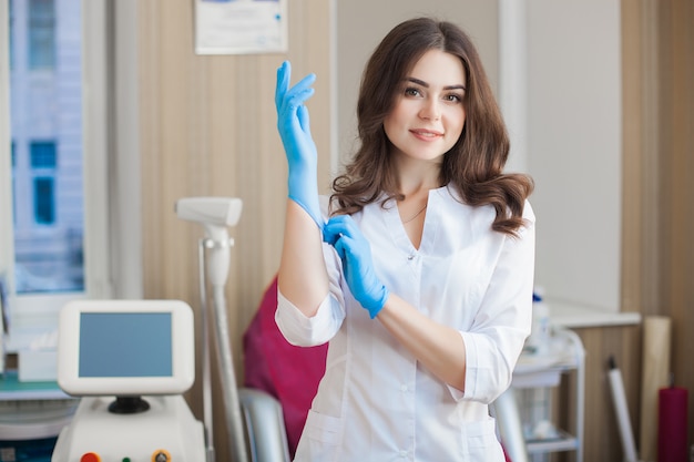 Giovane femmina attraente medico al chiuso. Ritratto della donna che indossa uniforme medica nella clinica. Medico con attrezzatura medica. Cosmetologo nel suo salotto