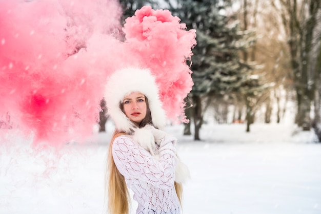 Giovane femmina caucasica in maglione con fumogeno rosso sulla giornata invernale di neve