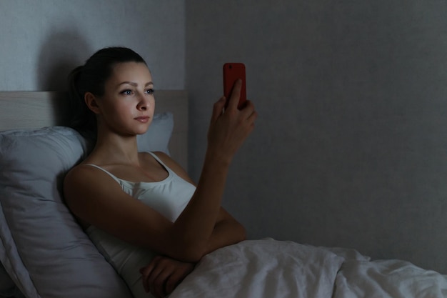 Giovane femmina che fissa in modo avvincente il suo smartphone a tarda notte nel suo letto