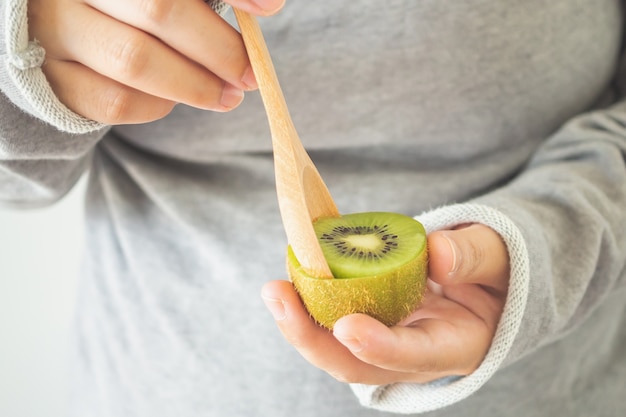 Giovane femmina che mangia kiwi maturo con un cucchiaio di legno