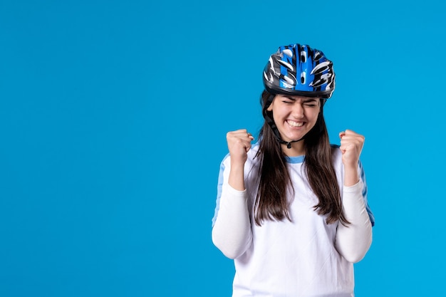 Giovane femmina di vista frontale in vestiti di sport con il casco sulla parete blu