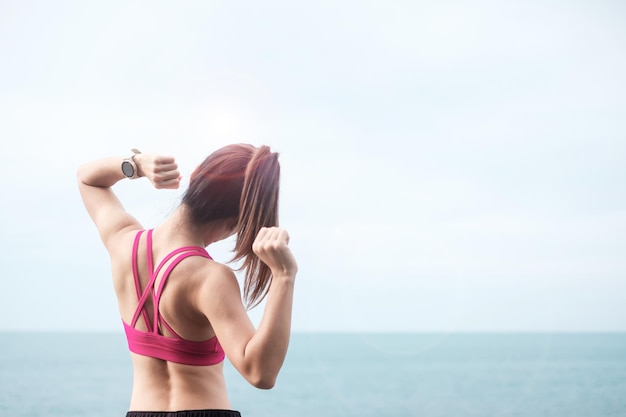 Giovane femmina fitness in abiti sportivi che allungano il corpo contro la vista sull'oceano, esercizio di donna sana al mattino. Concetti di allenamento, benessere e work life balance